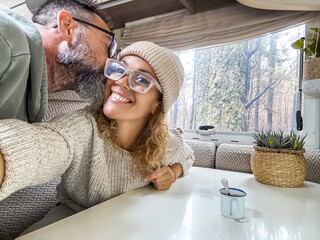 Wall Mural - Beautiful couple exchanging kisses in a camper taking photos with their cell phones and smiling. Husband and wife enjoy their holiday in the forest happily.