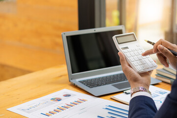 Wall Mural - Young Asian male businessman is pressing a calculator to calculate income, taxes and expenses, credit card bill for payment or payday at home. Close-up pictures