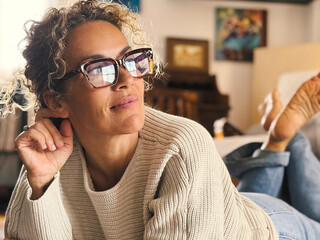 Wall Mural - One dreaming middle age female lay down on the floor at home looking outside in the air with an open computer laptop. Booking travel vacation online. Indoor relax leisure activity. Adult woman think