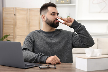 Canvas Print - Medical drops. Young man using nasal spray at table indoors