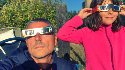 Canvas Print - Father and daughter looking at the sun during a solar eclipse on a country park, family outdoor activity