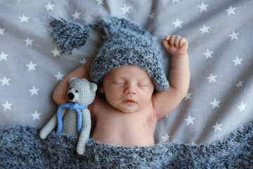 Poster - Cute newborn baby in warm hat with toy sleeping on bed, top view