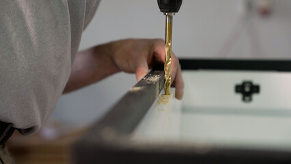 A craftsman drills a hole in a wooden board with a drill. Assembling furniture, close-up of a craftsman drilling a hole in the furniture.