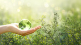 Fototapeta Kwiaty - Earth Day or World Environment Day, environmentally friendly concept. Crystal glass globe ball in human hand on green leaves background. Save planet and protect nature, sustainable lifestyle theme.