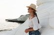 Young carefree woman in straw hat posing on white stones on rocky shore