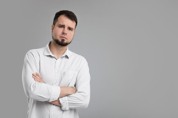 Wall Mural - Portrait of sad man with crossed arms on grey background, space for text