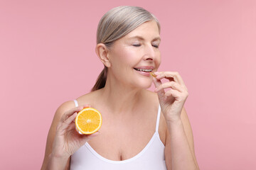 Canvas Print - Beautiful woman with half of orange taking vitamin capsule on pink background