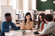 © Mediaphotos - International group of students sitting at table in college library and studying together with focus on young Asian woman