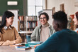 © Mediaphotos - Portrait of young male student with genuine smile enjoying schoolwork sitting at table with friends in library