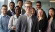 in the office, business people stand in front of each other and smile at the camera. a diverse group with a young man as the leader wearing glasses standing on a grey background looking at the viewer