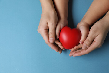 Wall Mural - Mother and her child holding red decorative heart on light blue background, top view. Space for text