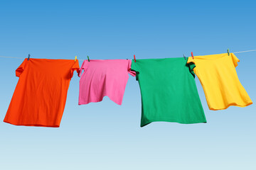 Wall Mural - Colorful t-shirts drying on washing line against blue sky, low angle view