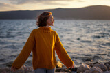 Fototapeta  - Smiling young woman in a yellow sweater looking at view at sunset enjoy sunshine.
