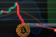 Bitcoin gold coin and defocused downward graph in dark background.