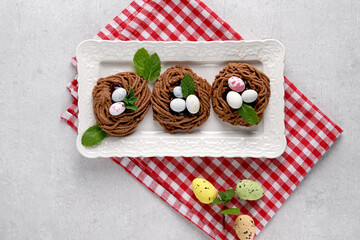 Easter chocolate cookies in the shape of Nests with sweet eggs on white plate on red napkin with mint leaves. top view