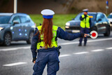 Fototapeta  - Policjantka ruchu drogowego z lizakiem podczas zatrzymania pojazdów na drodze z tarczą do zatrzymywania.

