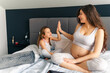 © DusanJelicic - Pregnant mother and her daughter high five each other while sitting on the couch, the tablet is in front of them and mom's belly is exposed