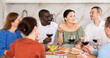 © JackF - Casual evening where multiethnic group of cheerful carefree adult friends sharing wine, dining together, and chatting in cozy home kitchen
