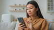 © Yuliia - Korean chinese multiracial woman use smartphone application surfing internet social media pensive Asian housewife girl in kitchen typing mobile phone message buy goods online order delivery at home