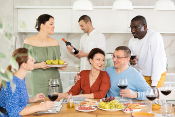 Wall Mural - Multiethnic women and men friends talking and drinking wine in the kitchen