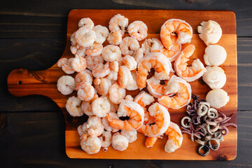 Wall Mural - Poached Seafood Arranged on a Wooden Cutting Board: Cooked small and large shrimp, sliced squid, and scallops on a wood chopping board