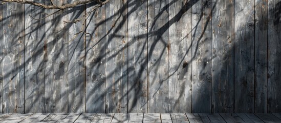 Wall Mural - The wooden wall has a shadow of a tree trunk and twig pattern. The grey wood blends with the natural landscape of grass and forest, creating a picturesque scene on the bedrock