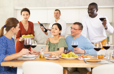 Wall Mural - Multicultural female and male friends chatting and drinking wine at table