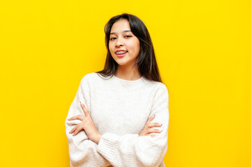 young cheerful asian woman with braces smiling with arms crossed on yellow isolated background, portrait of korean girl in studio