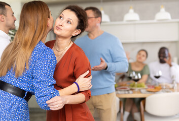 Wall Mural - Two women friends greet each other when meeting at party in kitchen