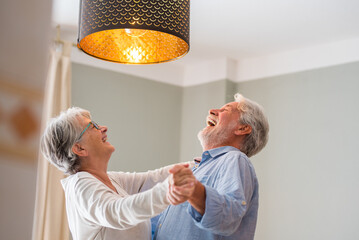 Canvas Print - Joyful active old retired romantic couple dancing laughing in living room, happy middle aged wife and elder husband having fun at home, smiling senior family grandparents relaxing bonding together.