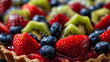 a close-up of a vibrant fruit tart adorned with glossy strawberries, kiwi slices, raspberries, and blueberries.