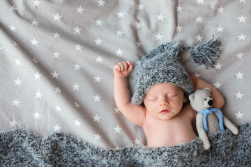 Poster - Cute newborn baby in warm hat with toy sleeping on bed, top view. Space for text