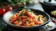 A vibrant dish of Pad Thai with juicy shrimp, garnished with fresh herbs and chili, served on a rustic ceramic plate.