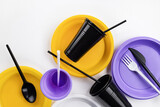 Fototapeta  - A set of disposable plastic tableware in lilac, yellow and black colors. Ecology and plastic waste recycling concept