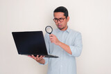Fototapeta  - Adult Asian man looking his laptop through magnifying glass