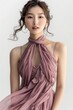 Portrait of a pretty young woman super model of Korean ethnicity draped in an ethereal pink chiffon gown with a halter neckline, gathered waist, and cascading ruffles