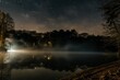 Starry night over a tranquil lake with mist and smoke rising from the water.