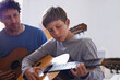 © M S/peopleimages.com - Learning, guitar and child with teacher for music, lesson and development of skill with instrument. Playing, practice and man helping kid in education as musician mentor in acoustic sound on strings