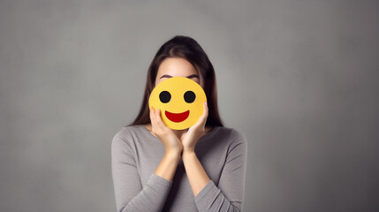 Woman covering face with heart eyes emoji on grey background