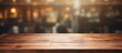 A hardwood plank table sits empty in a bar, surrounded by a blurry background of tints and shades. The wood flooring adds warmth to the horizon