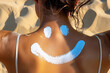 Close up of woman's tan back and neck with drawing of smiling face made from sunscreen cream