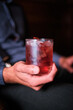 A close-up image capturing a moment of someone holding a glass of cherry cocktail, garnished with a cherry, at a well-lit bar