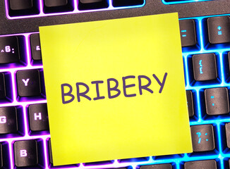 Wall Mural - Word BRIBERY written on a yellow sticker on a colored backlit keyboard