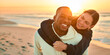 Casually Dressed Loving Couple With Man Giving Woman Piggyback Ride On Beach Shoreline At Sunrise