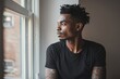 Calm african american man in black t-shirt with tattoo on arms looking through window
