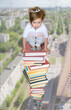 © Pavel Losevsky - Collage with girl sitting on high stack of books against background of city panorama from birds eye view