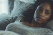 A beautiful black woman lying on her bed with an expression of sadness and tiredness. A black lady wearing comfortable pajamas. A contemplative female. Sleepiness. Melancholy. Reflective mood.Brunette