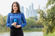 © Pavel Losevsky - Young woman reporter stands with microphone against pond, green trees and skyscrapers.