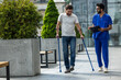 Man with crutches and a male nurse talking friendly on a walk