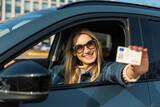 Fototapeta Mapy - smiling young woman showing her new driver license out of car window after successful test at driving school